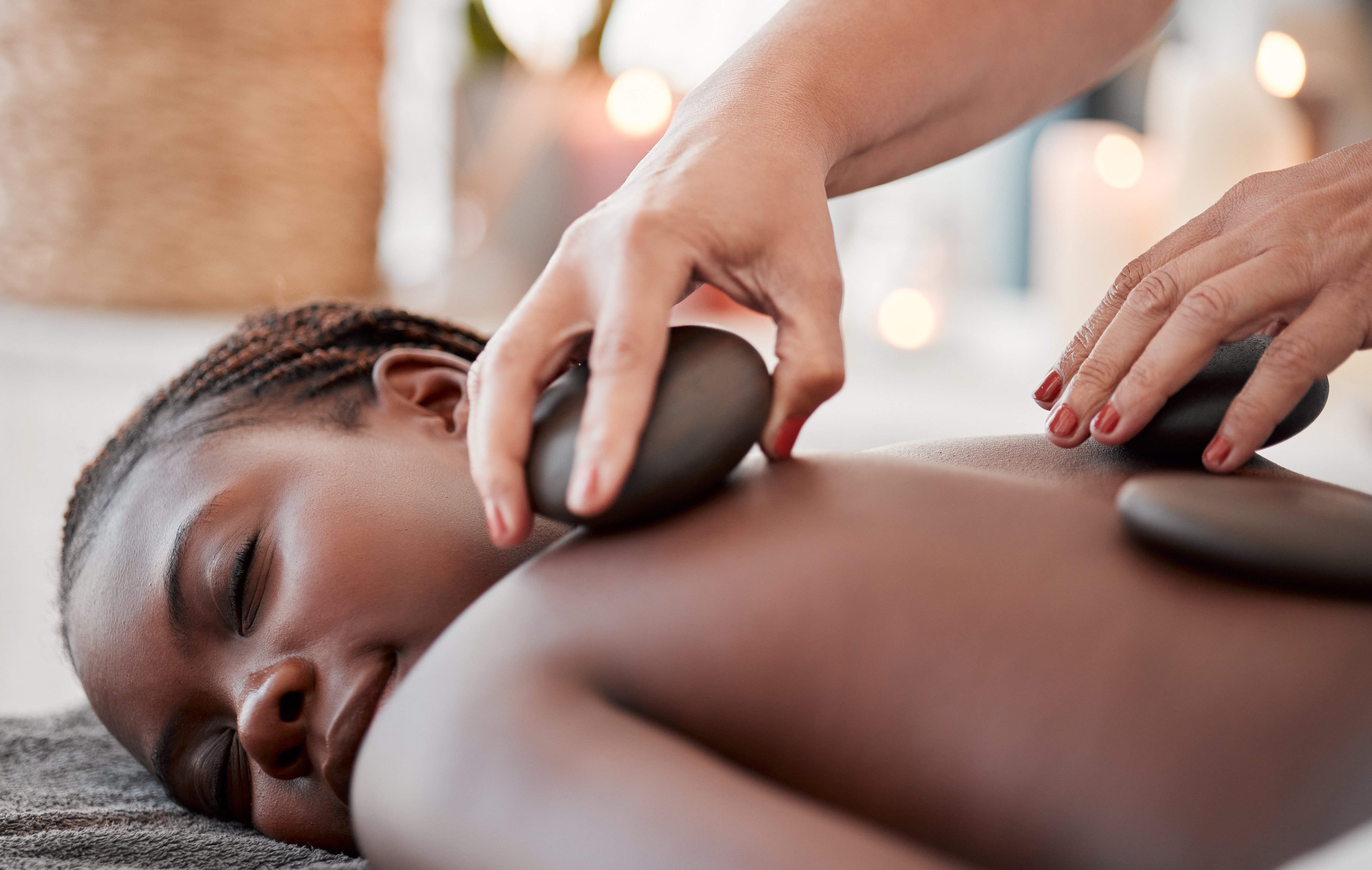 Black woman, hot stone massage, spa and hands of masseuse, holistic and wellness, therapy and treatment. Health, peace of mind and self care with zen, stress relief for people and back skin detox